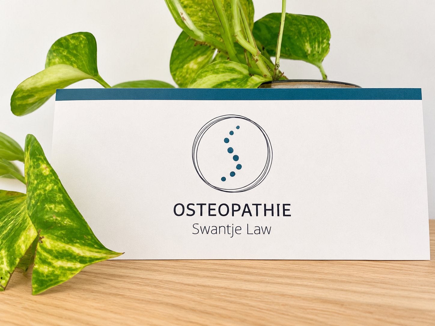 Gift voucher card of Praxis für Osteopathie Swantje Law with the logo, in front of a houseplant